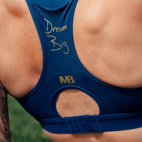 Blue sports bra with 'Dream Big' text and NB logo on a person against a blurred green background