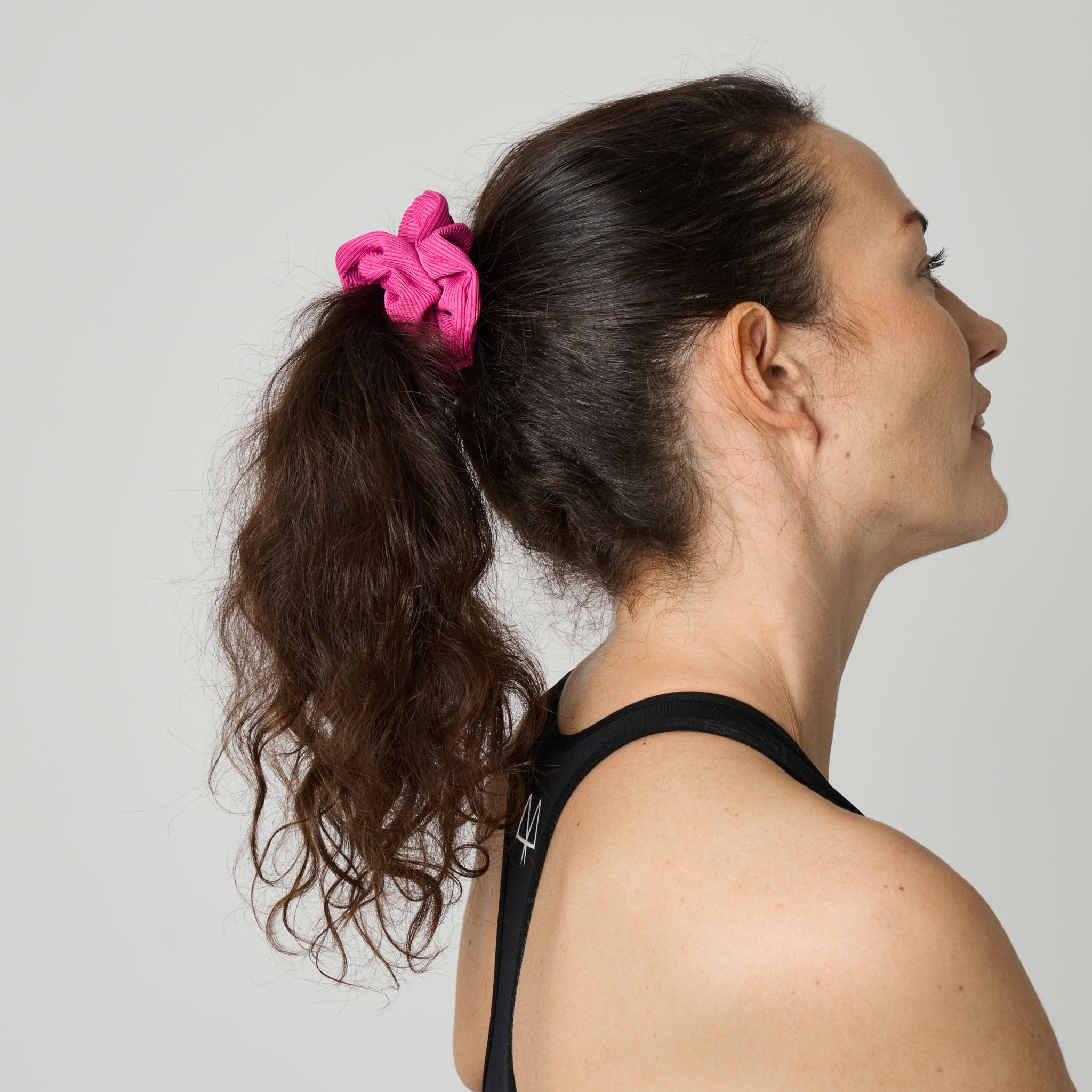Woman with a pink scrunchie in her hair against a plain background