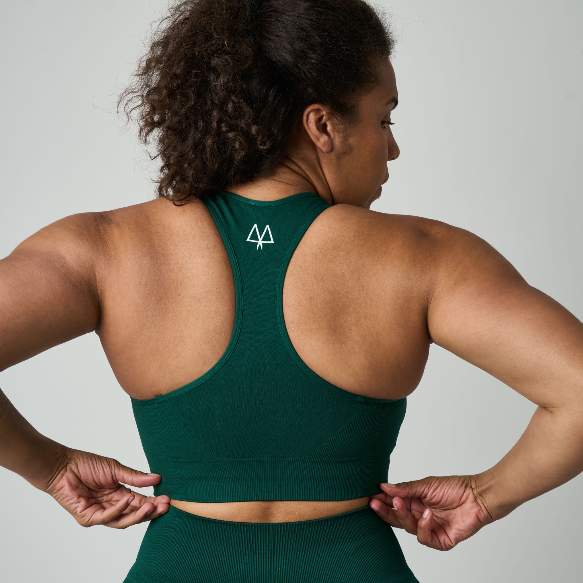 Woman wearing a green sports bra with a logo on a plain background