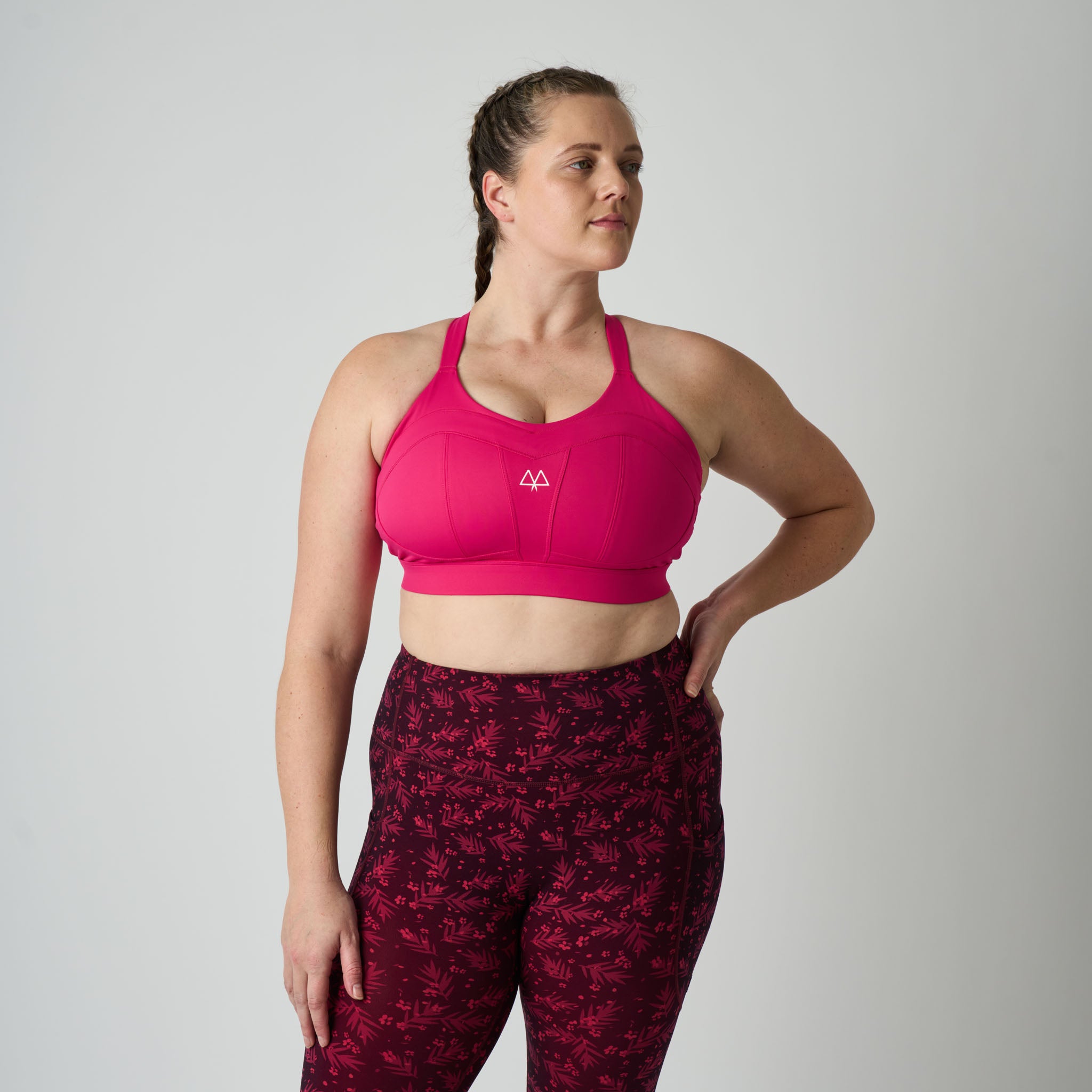 Woman wearing a pink sports bra and maroon patterned leggings on a gray background