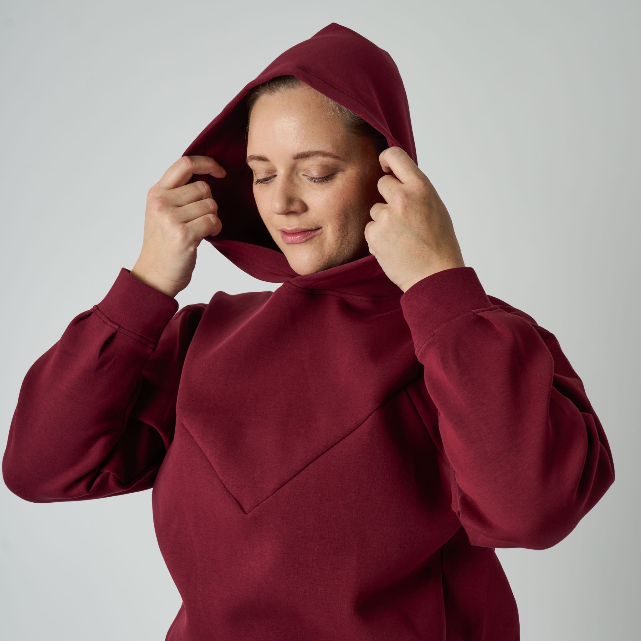 Woman wearing a burgundy hoodie against a plain background
