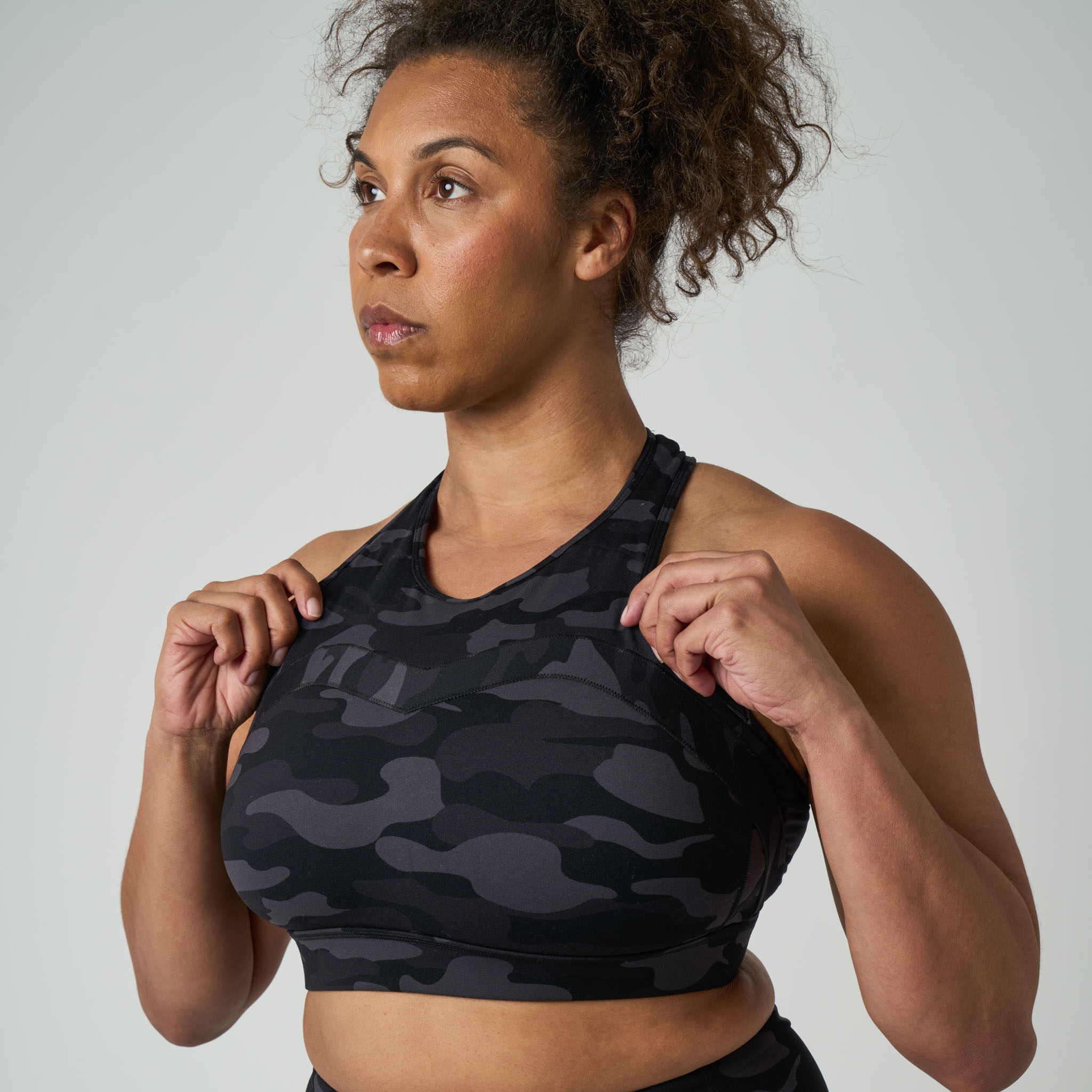 Woman wearing a black camouflage sports bra against a plain background