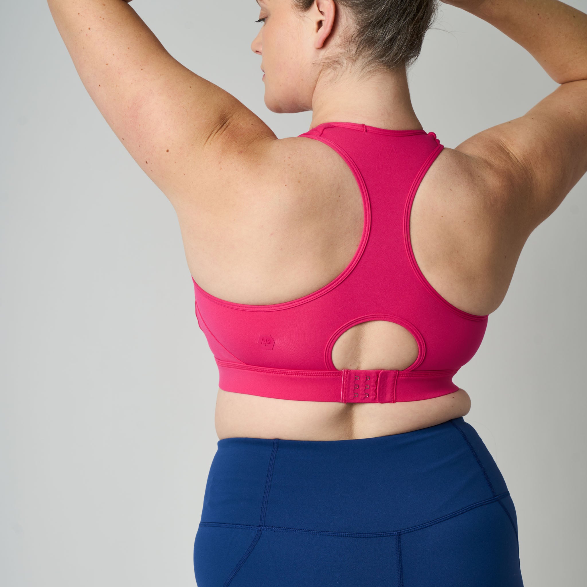 Person wearing a pink sports bra and blue leggings on a gray background