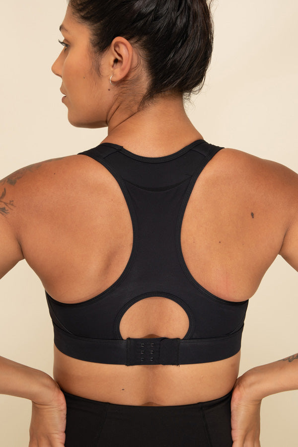 Close up view of a Woman wearing a Black Sports Bra from the back. The rear pocket and hook and eye clasp on the bra can be seen.