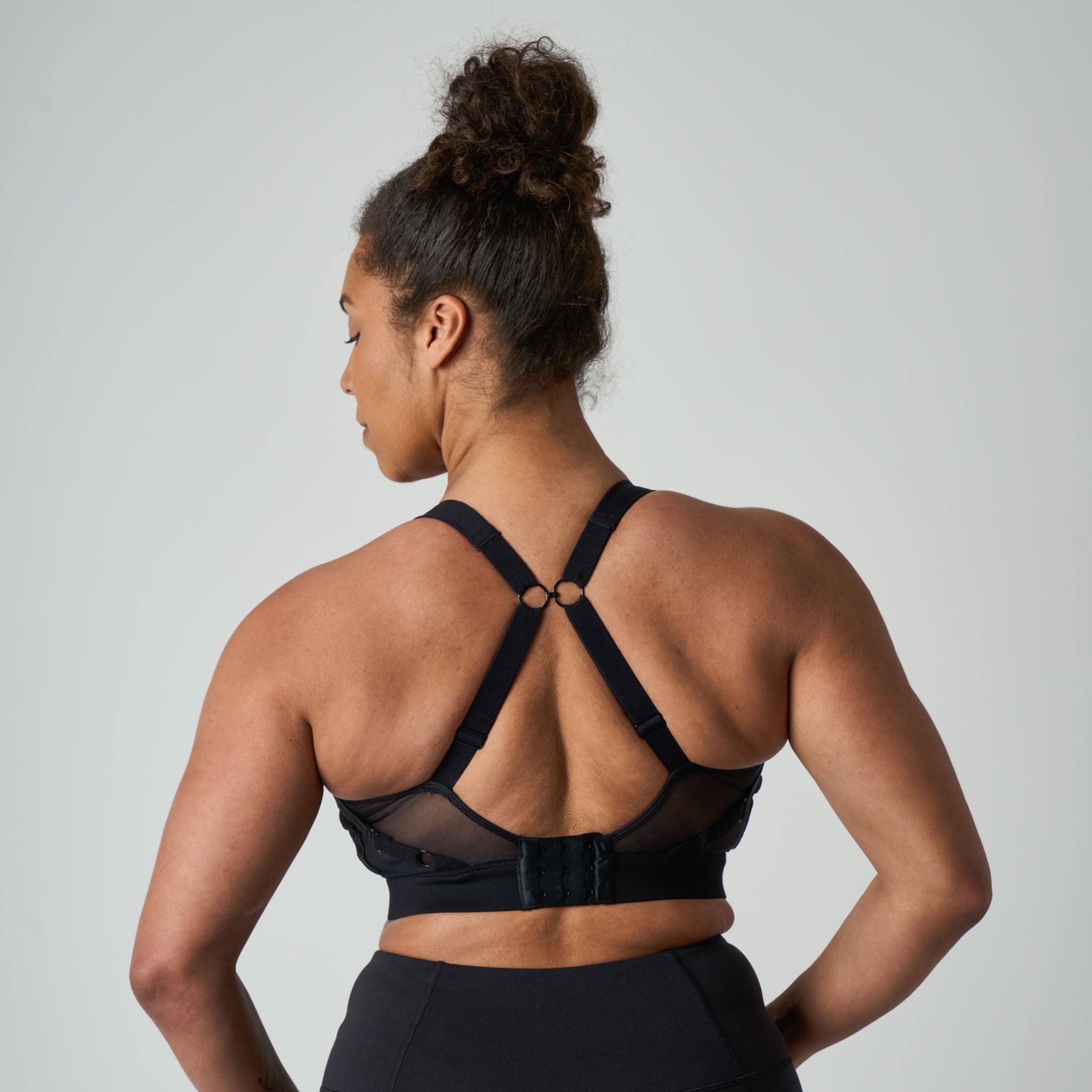 Woman wearing a black sports bra with straps on a plain background
