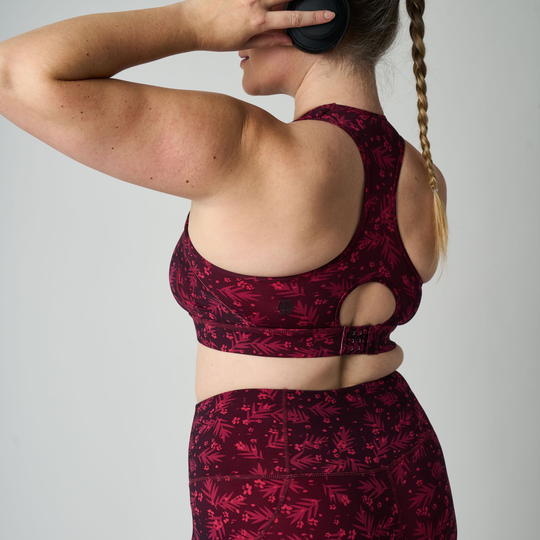 Woman wearing a maroon sports bra and leggings with a pattern on a plain background